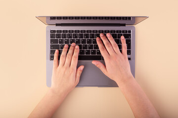 Person using a laptop computer on beige background. Flatlay, concept freelance, shopping and work place