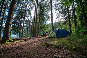 Men light a fire. Arrangement of a camp for recreation in the woods. Cars with luggage and equipment in the background, sunset. Smoke from the fire.