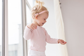 Cochlear implant for baby. Deaf child with hearing aid plays in living room. Health care and...