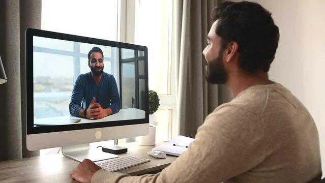 Indian dark-haired man using computer for video call sitting in home office. Brunette male entrepreneur talking with male colleague, taking classes, studying on the distance