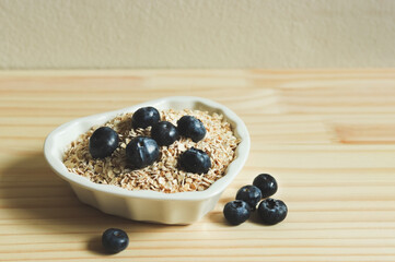 breakfast with oat or granola in heart shape bowl, fresh blueberries on wooden table. Healthy breakfast concept.