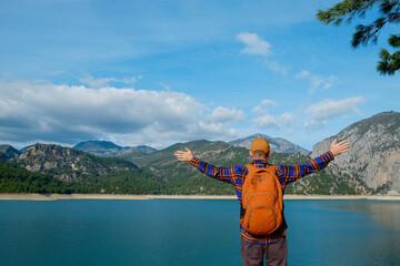 Male traveler wearing flannel shirt and a backpack enjoying beautiful view of a mountain lake. Man experiencing spiritual uplifting from being alone in nature. Scenic background, copy space, back view