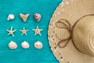 Flat lay straw hat beside seashells, stones and starfish on aquamarine background 