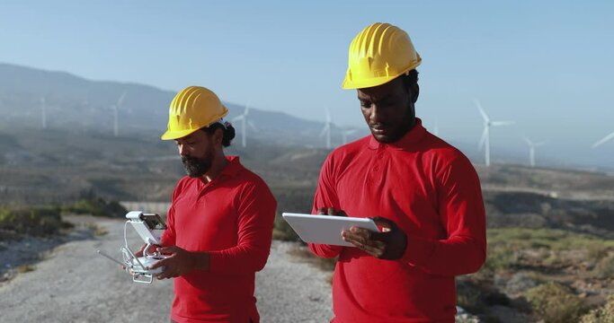 Multiracial engineer men working together on a windmill farm using digital tablet and drone - Renewable energy concept