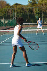 African american female player playing tennis game with caucasian competitor at court on sunny day