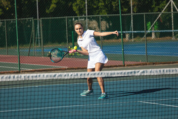 Full length of young female caucasian player hitting ball with racket at tennis court on sunny day
