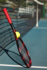 Badkamer foto achterwand Ball with red racket leaning on tennis net at court during sunny day © WavebreakMediaMicro