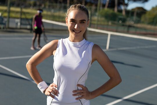 Portrait of smiling beautiful caucasian female tennis player standing with hands on hip at court