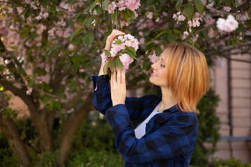 Fototapeta premium Young woman near sakura blooming tree. Pink flowers, spring and youth concept. Stylish girl smiling