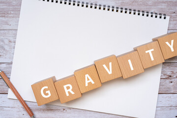 重力・引力のイメージ｜「GRAVITY」と書かれた積み木、ノート、ペン、手