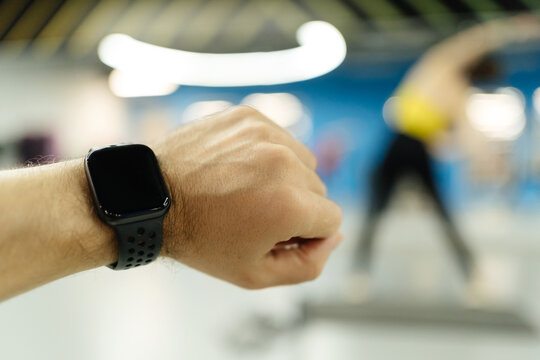 man's hand with a smart watch and a monitor against the background of a gym and training people in bokeh.