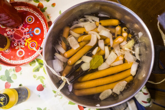Hot dogs staying warm in hot water with bay leaves and onions on a buffe table.
