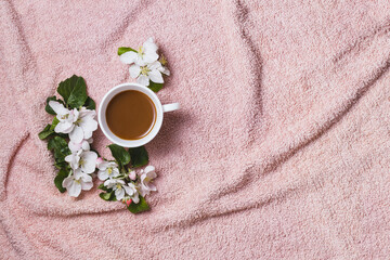 Obraz na płótnie Canvas Apple blooming with white cup of coffee on fur pastel pink towel, flat lay. Good morning background with spring flowers copy space.