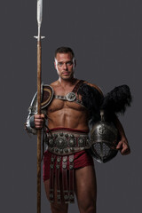 Fototapeta premium Studio shot of antique gladiator holding helmet plumed with black feathers and long spear.