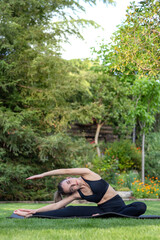 Vertical view of beautiful woman practising sport and yoga sitting on the grass ground in the grarden
