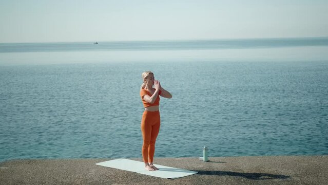 Yoga woman near the sea. Spiritual practice in nature. A woman is doing yoga on the seashore, doing asana salutation to the sun (surya namaskar). Calmness, meditation. Overall plan.