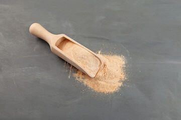 Date sugar in wooden scoop. No refined sugars. Natural date powder scattered on grey textured...