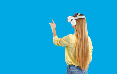 Back view of woman in VR glasses touch space or air with fingers. Millennial girl in virtual reality headset explore discover new horizons in modern device. Technology and innovation.