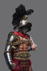 Shot of violent roman gladiator dressed in light armor and red cape against gray background.