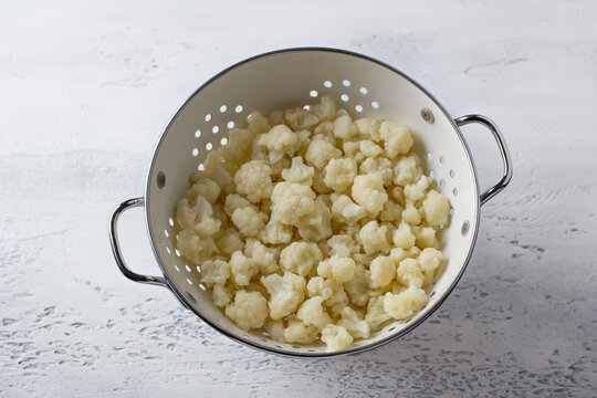 Colander with steamed cauliflower inflorescences on a light gray background. Cooking healthy homemade food