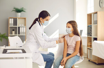 Kids getting shots at the hospital. Nurse at a new modern clinic giving an injection to a child in a face mask. Doctor giving a Covid 19 vaccine to a teenage girl who's wearing a mouth covering - obrazy, fototapety, plakaty