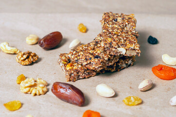 granola bars, dried fruits and nuts on craft paper with dried fruits and nuts scattered nearby. side view.