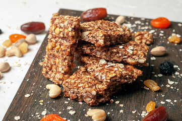bars of dried fruits, cereals and nuts with ingredients lying next to each other on a dark wooden board on a gray background close-up.