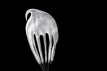whisk with whipped cream or whipped white on a black background, copy space.
