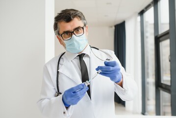 Fototapeta premium Mid aged male doctor wearing protective mask holding a syringe with vaccine.