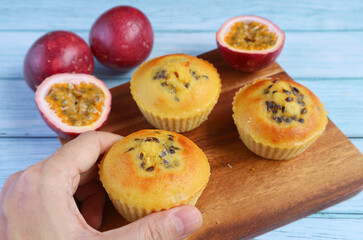 Hand Picking a Passion Fruit Muffin from Breadboard with Fresh Fruits Scattered on Light Blue...