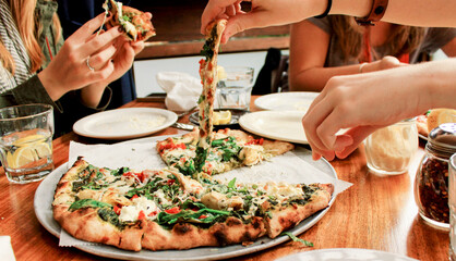 Sliced pieces of spinach greek style pizzas at a restaurant table gathered around by a group of women