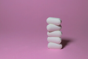 White pills stacked on pink surface