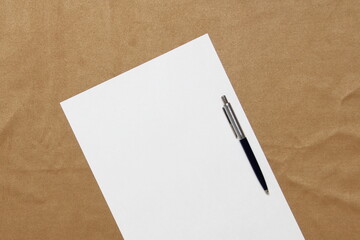 Template of white paper with pen lies diagonally on light brown cloth background. Concept of business plan and strategy. Stock photo with empty space for text and design.