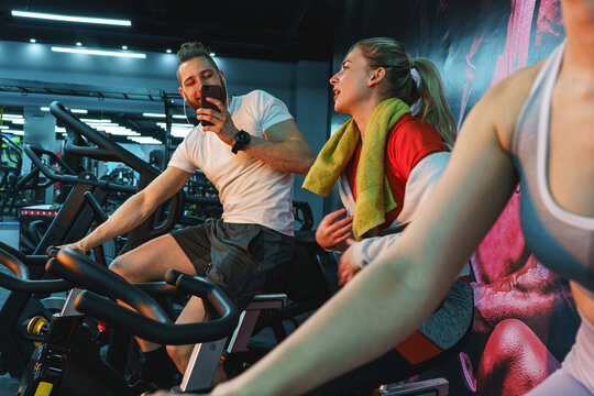 A young, handsome man works out during a spinning session on a cycling machine at the gym with his friends.
