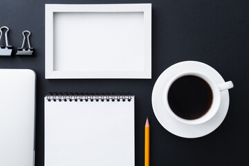 flat lay of fold back clips near notebook, frame and cup of coffee on black.