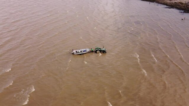 Aerial orbit shot of industrial tractor pulling boat out of River Plate in Argentina after accident