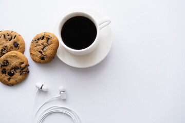 top view of cup of coffee near chocolate chip cookies and wired earphones on white.