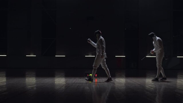 Two professional male fencers having a sabre fight in against dark background