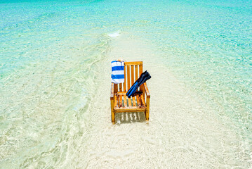 Fototapeta premium A wooden chair standing in the Indian Ocean with a towel, shell and flippers.