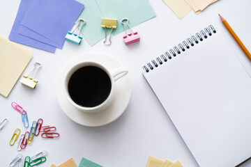 top view of cup of coffee near blank notebook and colorful stationery on white.