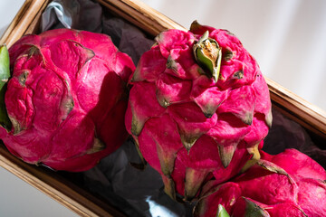 Three juicy ripe Thai whole pitahaya or dragonfruit in a wooden box on a white background.