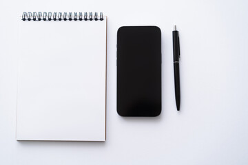 top view of mobile phone with blank screen near notebook and pen on white.