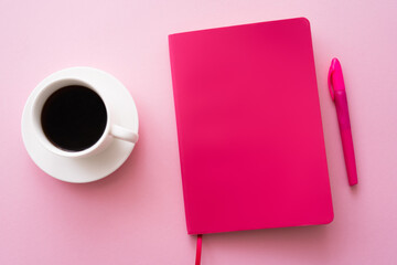 top view of pen near bright notebook and cup of coffee on pink.