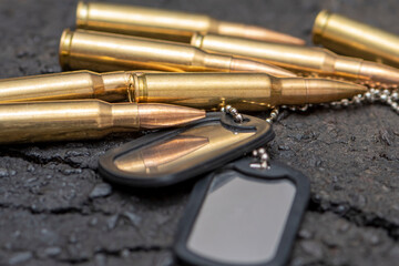 Live ammunition and army identification tokens on a textured background of cracked asphalt....
