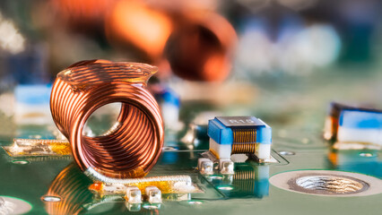 Orange wire winding of air-core coil and PCB electronic components in blurry background. Closeup of...