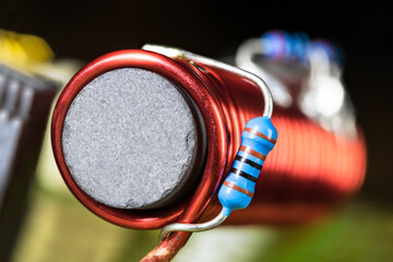 Cylindrical inductor with black ferromagnetic core wrapped by red wire on PCB detail. Closeup of...