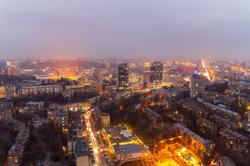 Fototapeta premium Ukraine, Kyiv – March 12, 2016: Aerial panoramic view on central part of Kyiv city from a roof of a high-rise building. Night life in a big city. Foggy and rainy weather. 