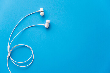 top view of white wired earphones on blue.