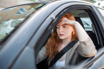 Fototapeta na wymiar Nervous female driver sits at wheel, has worried expression as afraids to drive car by herself for first time. Frightened woman has car accident on road. People, driving, problems with transport