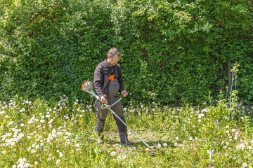 A man mows grass on his property with a gasoline trimmer